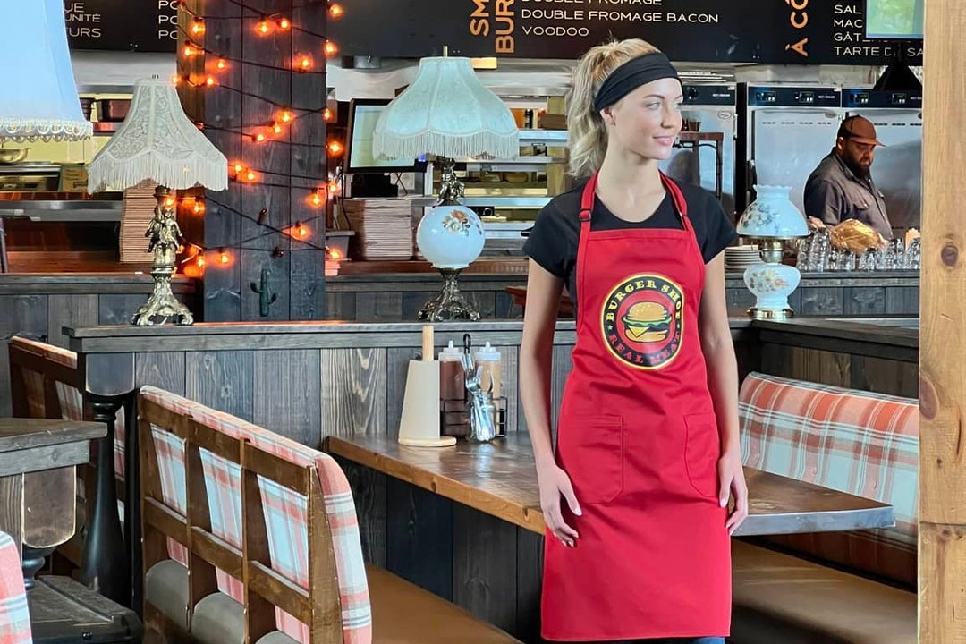 Jeune femme portant un uniforme et un tablier personnalisés avec le logo du restaurant pour lequel elle travaille. 